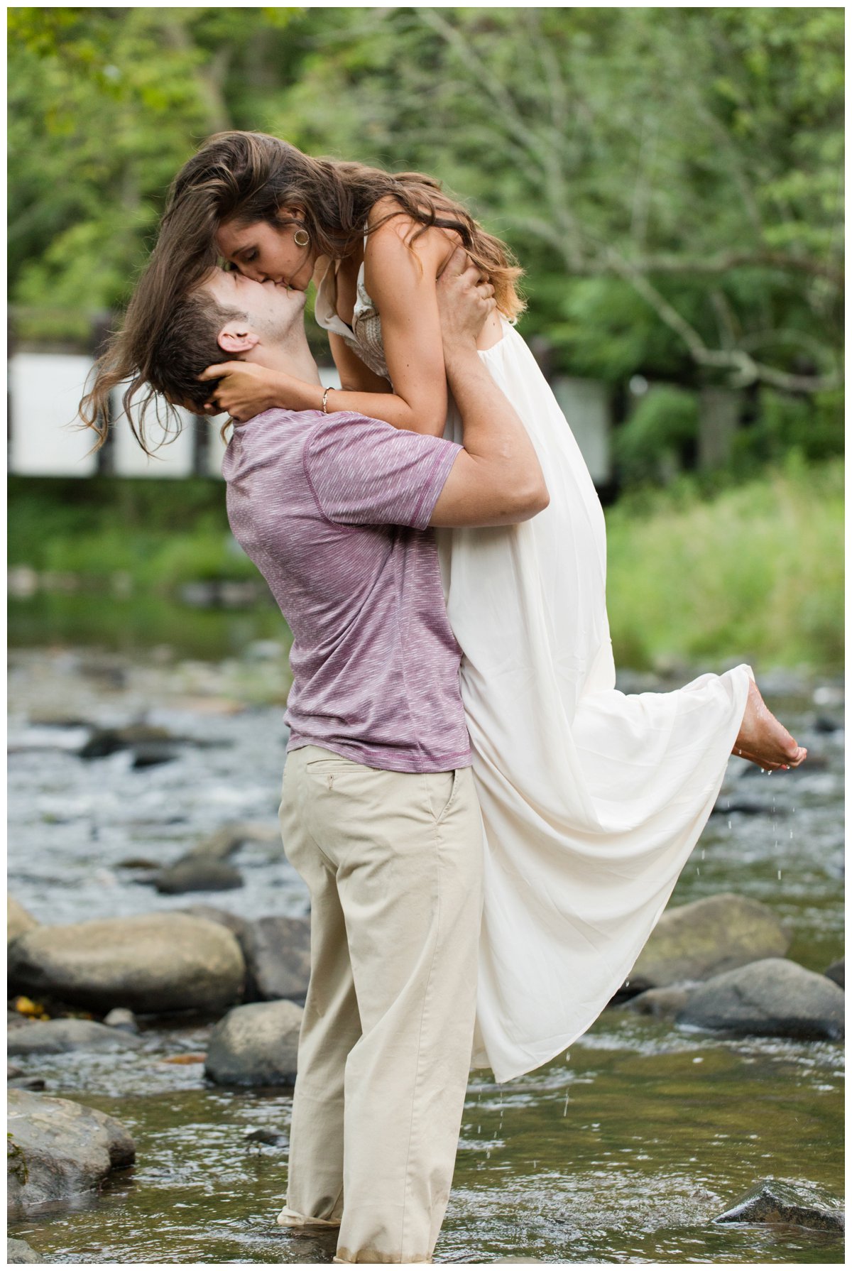 Jerusalem Mills Bohemian Engagement Photography in a stream in a white dress. He is lifting her and Kissing her. Water is dripping from her feet.